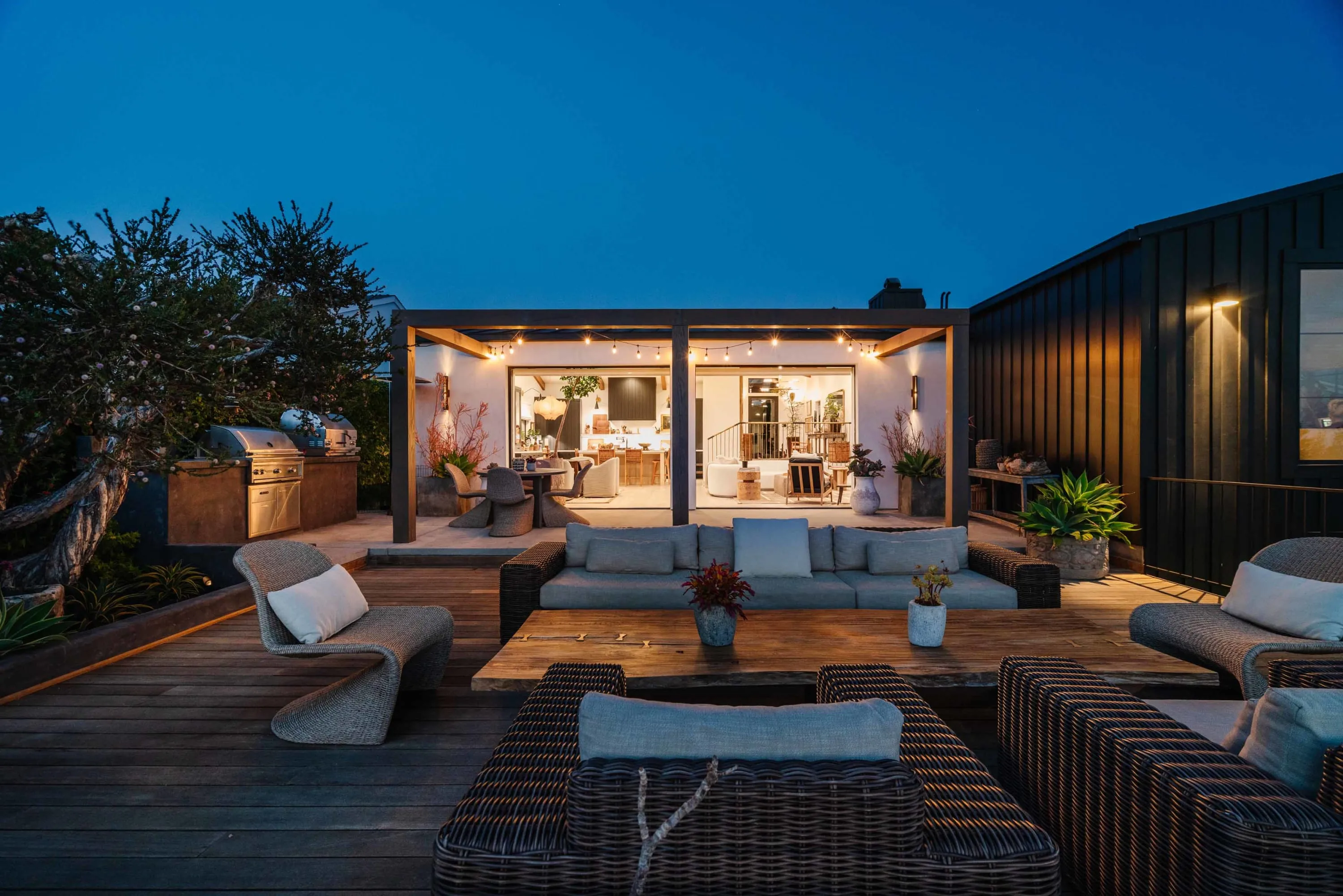Black modular home at dusk with a deck, outdoor kitchen and string lights
